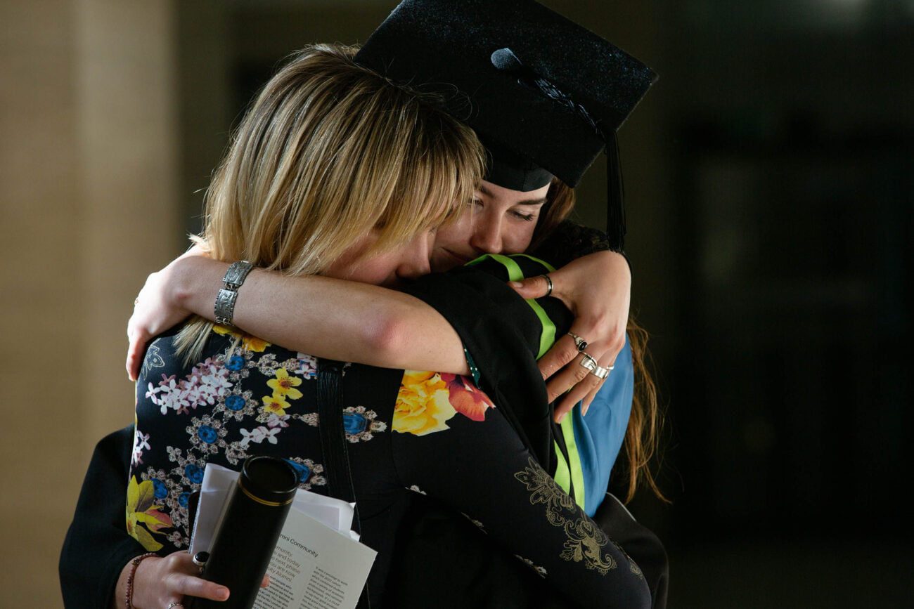 Graduation Event Photographer of Northeastern University Graduation Ceremony taking place at Senate House London - A candid photograph of a graduate receiving a hug from a friend after the Graduation Ceremony captured by Carmen Valino
